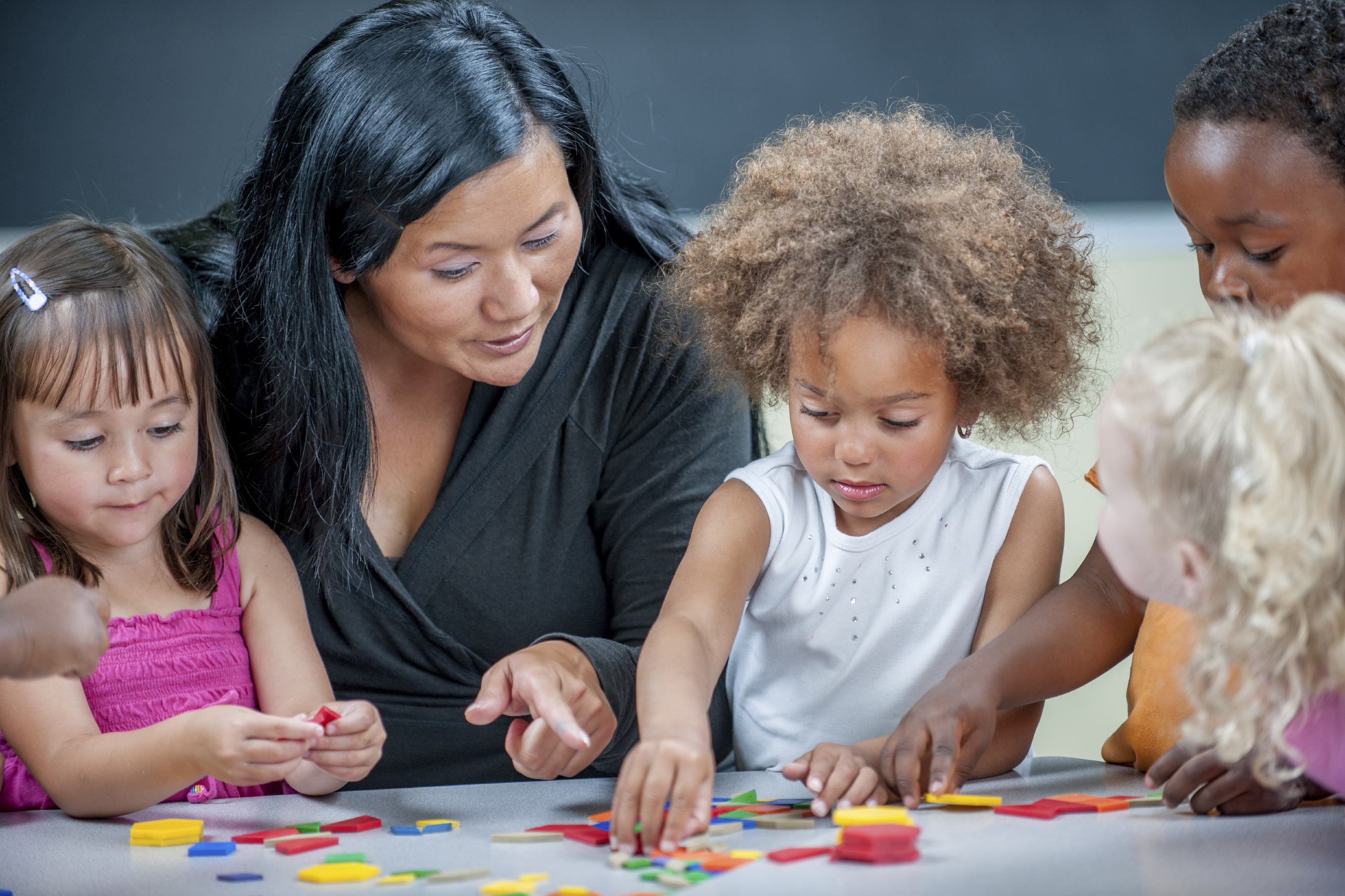 A multi-ethnic group of elementary age children are sitting at a table and are painting an art project.